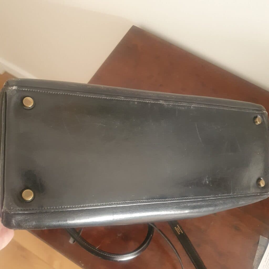 “Sac à main vintage de couleur noire en cuir avec poignée et bandoulière amovible, orné de ferrures dorées, présentant une usure visible et un aspect patiné”